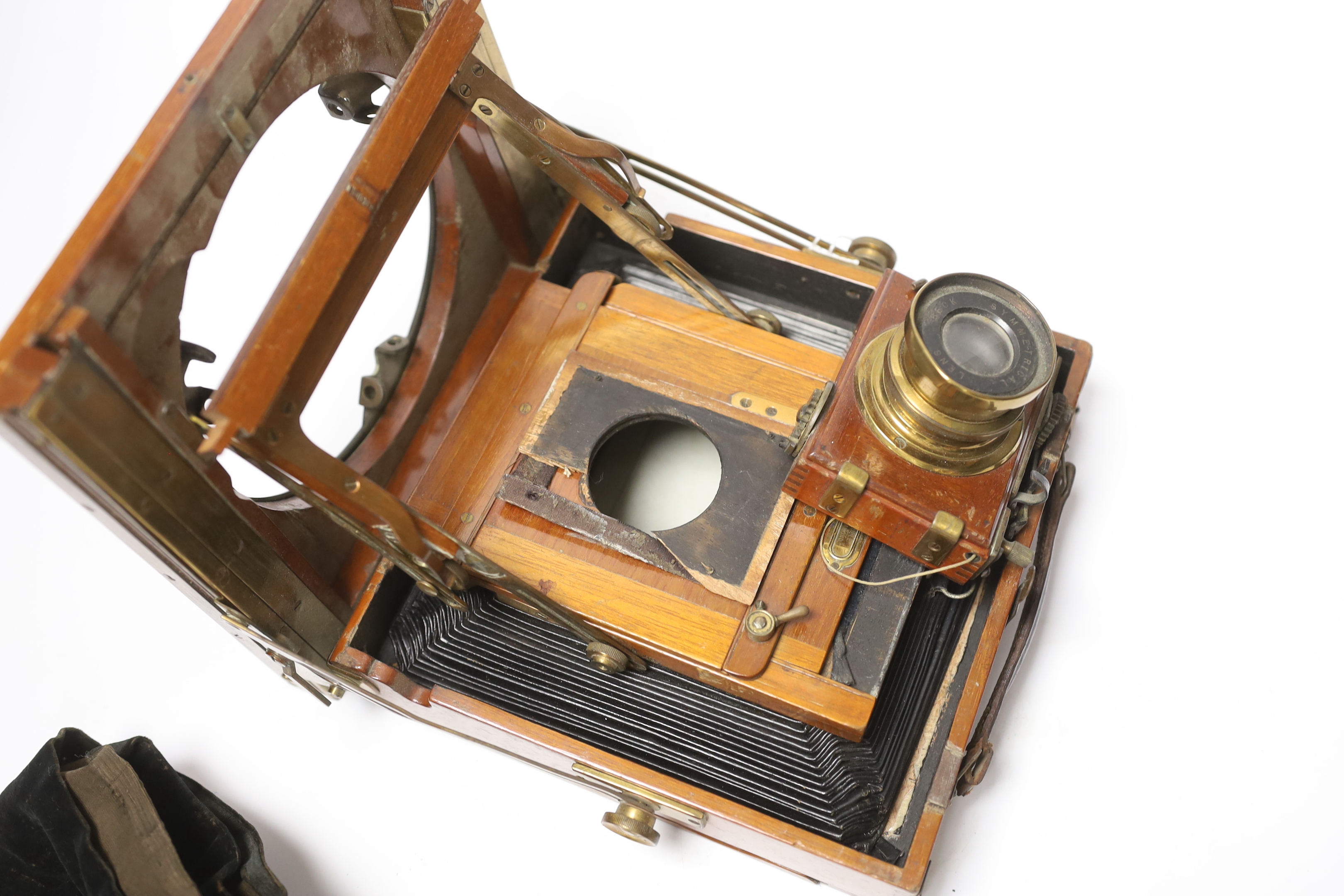 An early 20th century brass and mahogany half plate bellows camera with a lens and a shutter action by Thornton Pickard, on an oak tripod